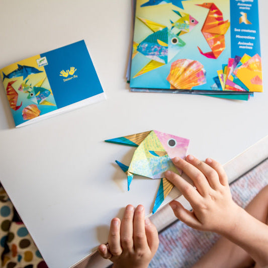 Child playing with a colorful paper fish on a table with children's books in the background