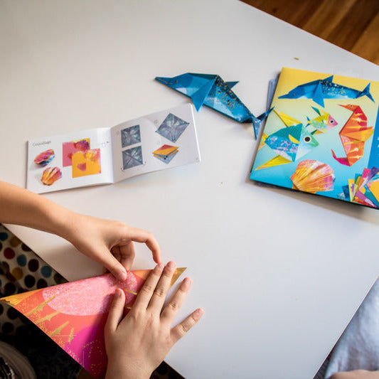 Two people making origami at a table with colorful paper and instructions.