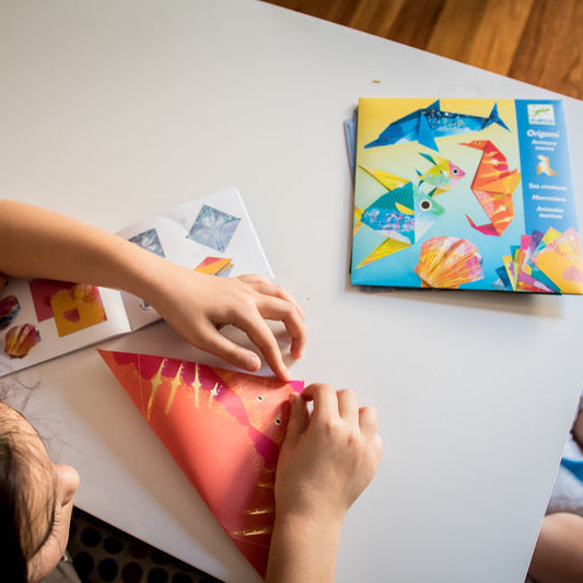 Child crafting with paper at a table, surrounded by art supplies