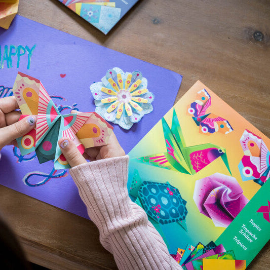Children's hands holding a colorful paper craft on a table with art supplies.