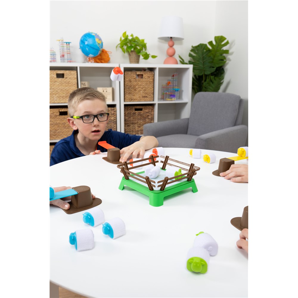 Child playing with a toy sheep and fence set on a table in a room with shelves and plants.