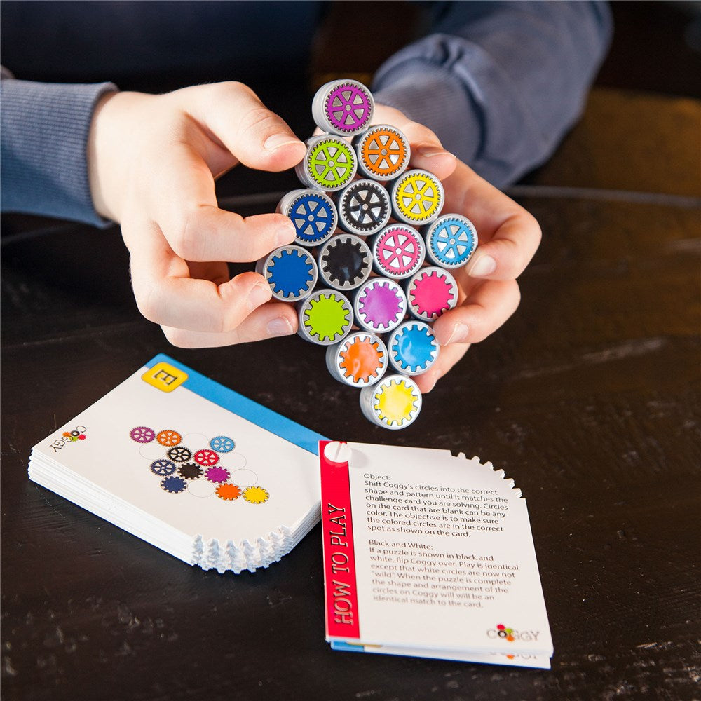Colorful gear-shaped toys held by a person with a 'How to Play' card on a dark surface.