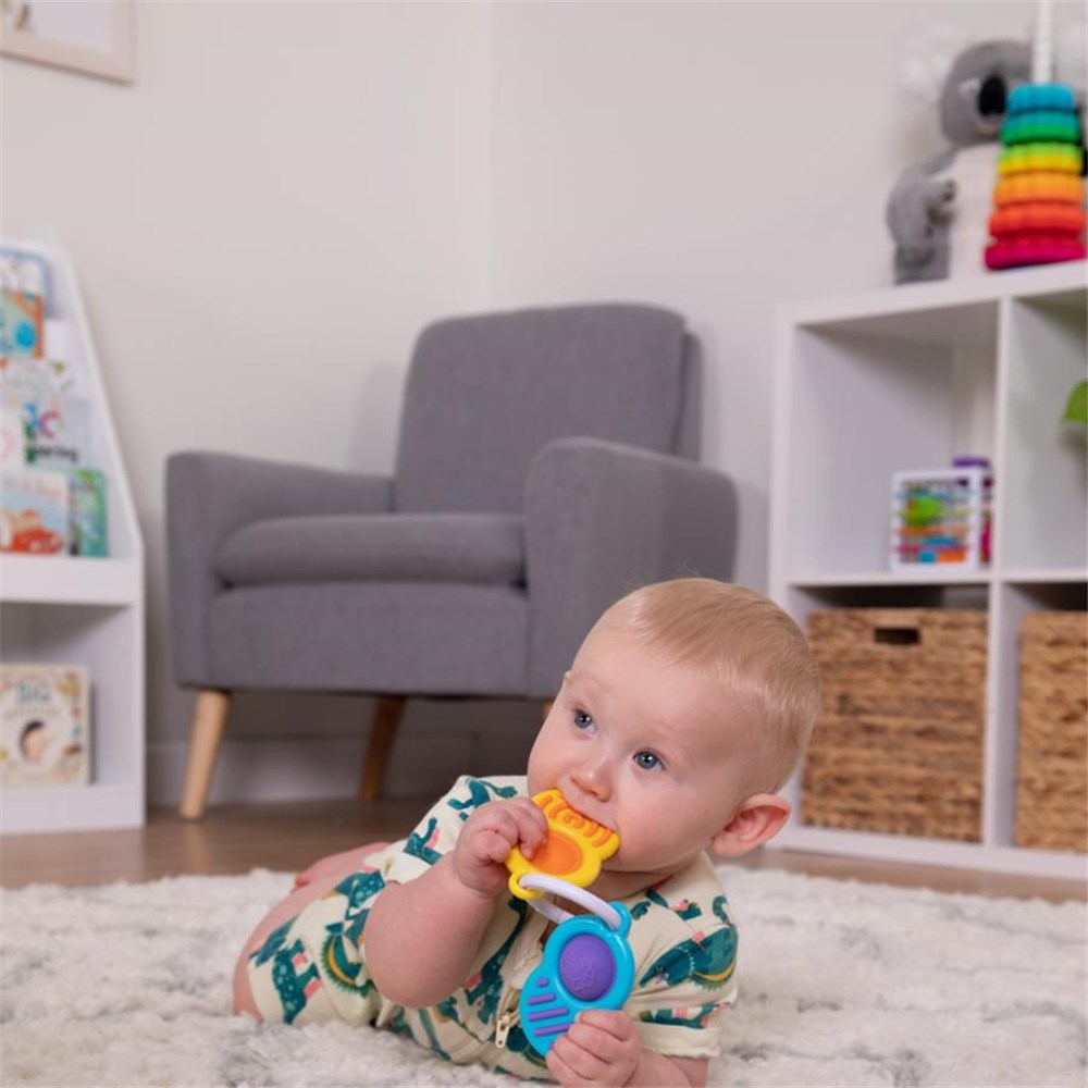 Baby playing with a colorful toy in a room with a gray armchair and shelves.