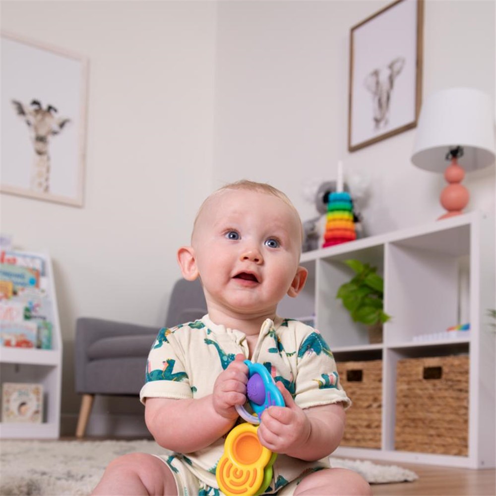 Baby sitting on the floor holding a colorful toy in a room with shelves and decor.