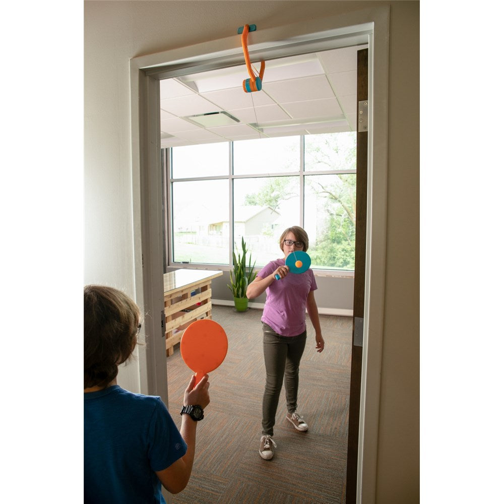 Two children playing with colorful paddles in a room with large windows.
