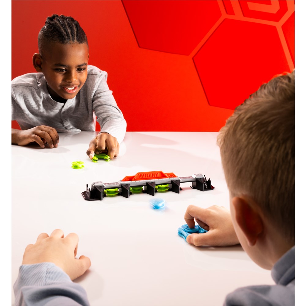Two children playing with toy on a white table against a red geometric wall.