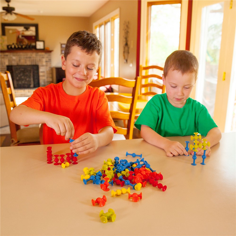 Two children playing with colorful building blocks at a table in a home setting.