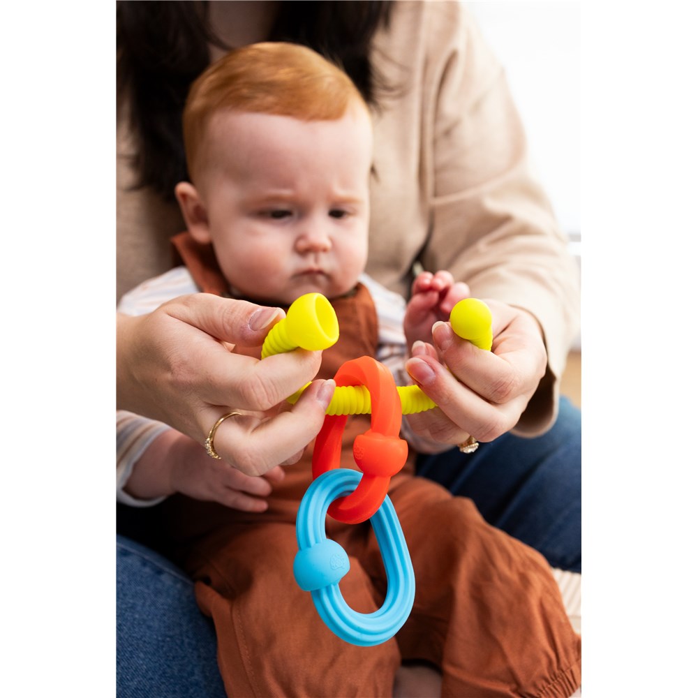 Baby holding a colorful teething ring with adult hands assisting