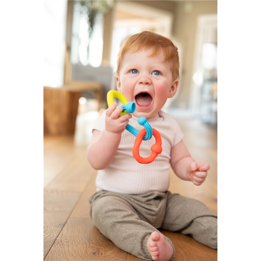 Baby sitting on a wooden floor holding a colorful teething ring.