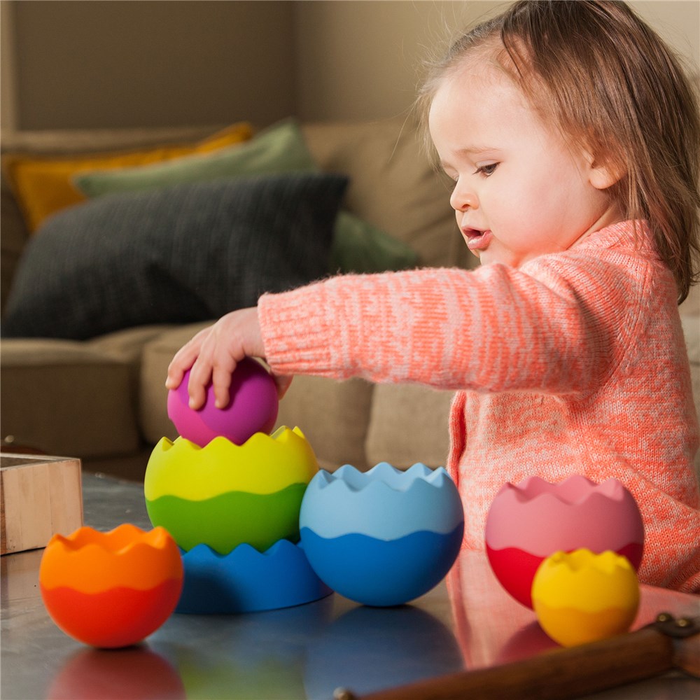 Child playing with colorful plastic eggs on a table in a living room setting.
