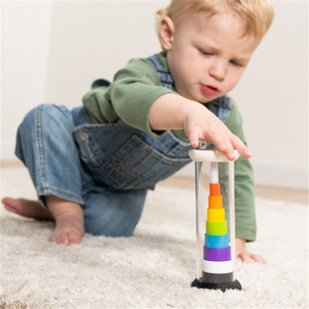 Child playing with a colorful tower toy on a carpeted floor.