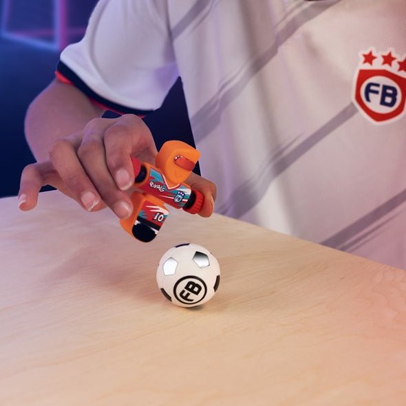 Child playing with toy cars near a soccer ball on a table with a dark background