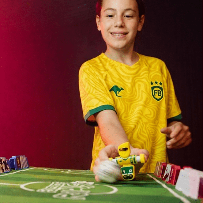 Child in a yellow sports jersey holding a toy car on a table with cards