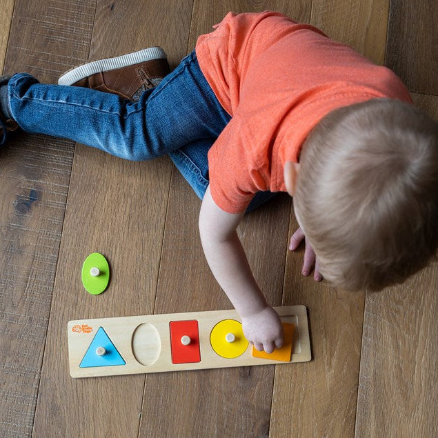 Child playing with a wooden shape sorting toy on a wooden floor