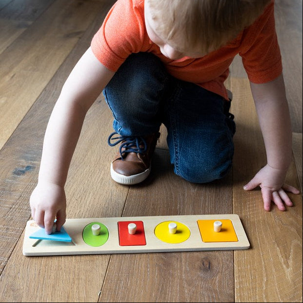 Child playing with a colorful sorting board on a wooden floor