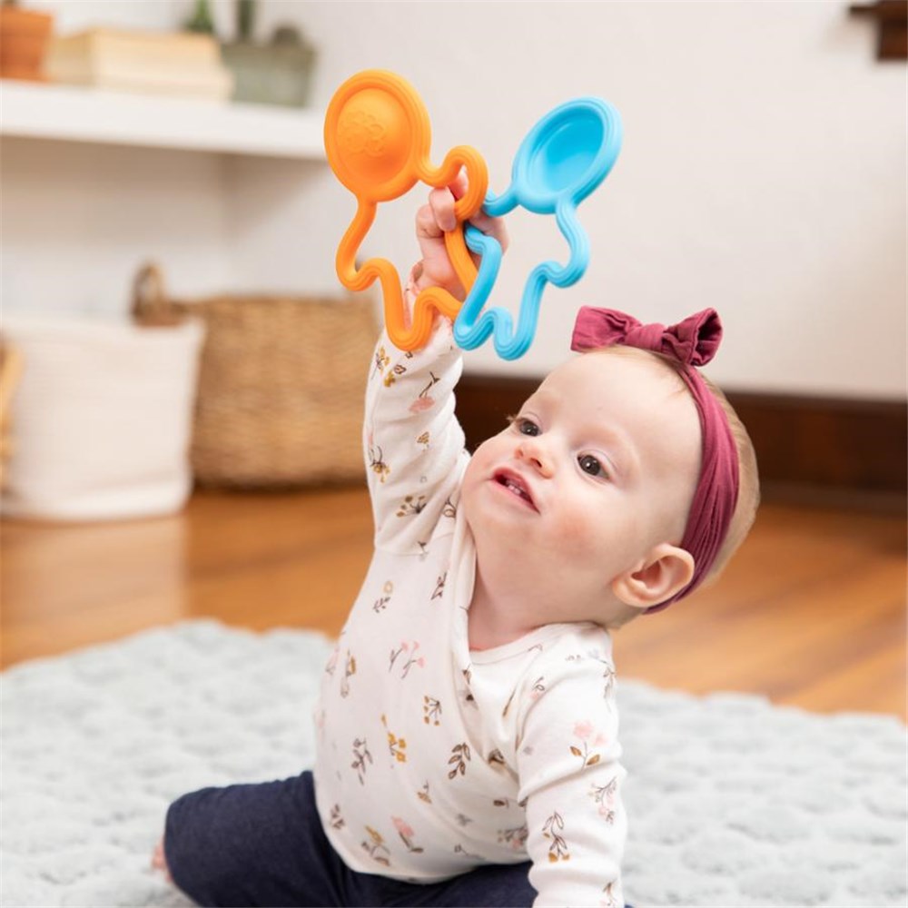 Baby playing with colorful rattles on a soft surface
