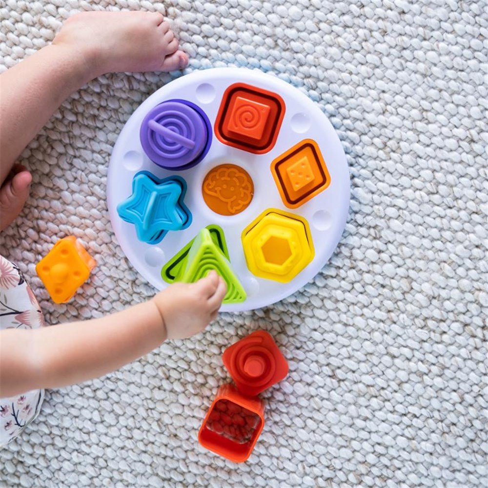 Colorful shape sorting toy on a textured carpet with child's hand reaching towards it.