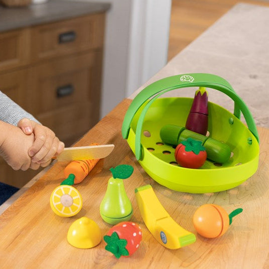 Child playing with toy vegetables and a cutting board on a wooden table.