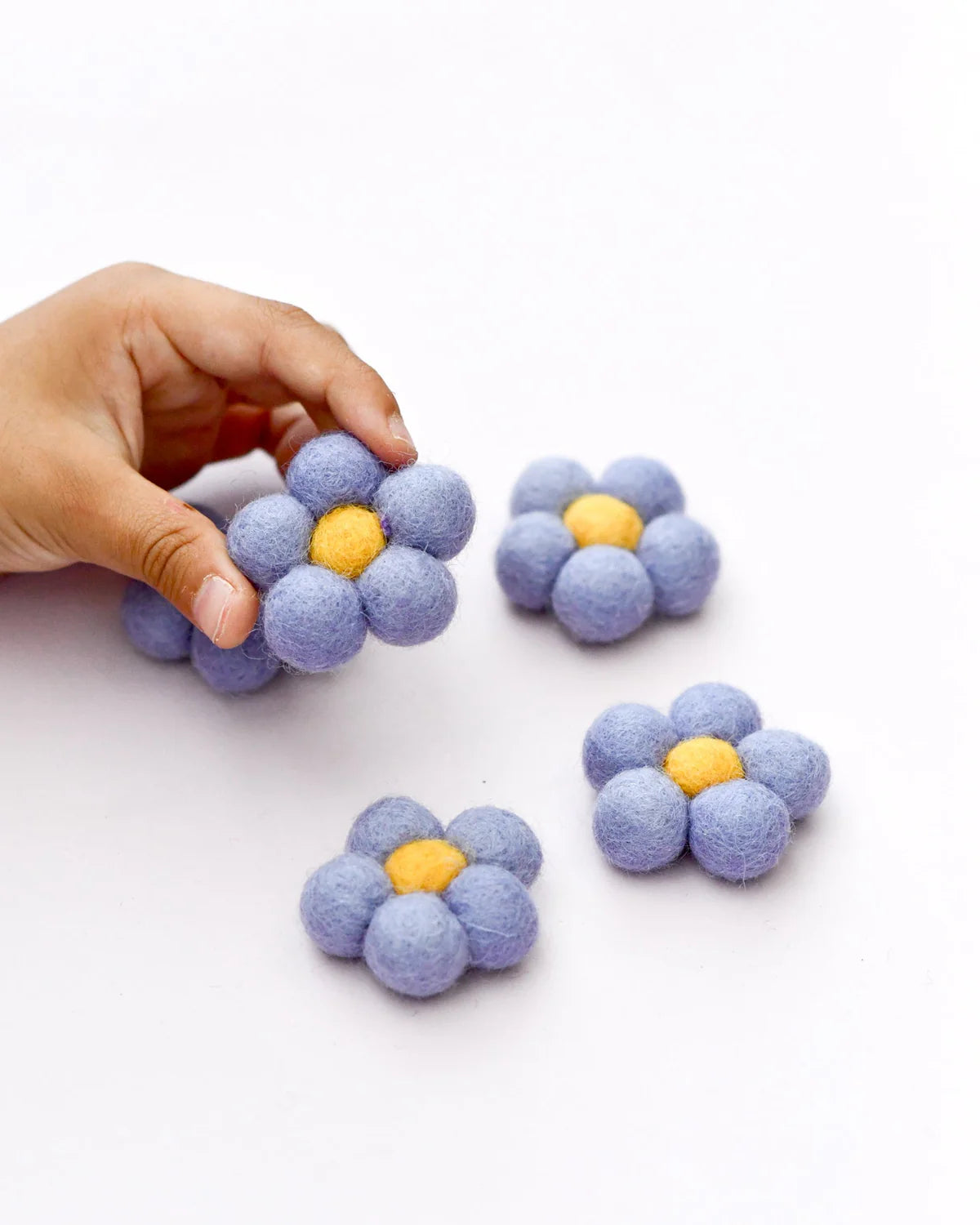 Hand holding a blue flower-shaped stress ball with yellow center on a white background