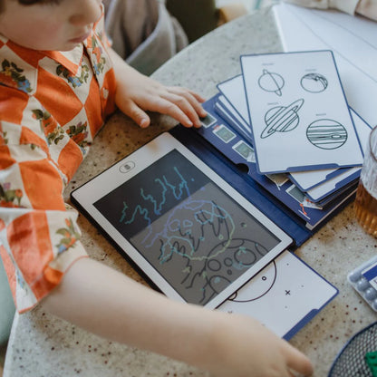 Child interacting with a small electronic device on a table with educational materials.