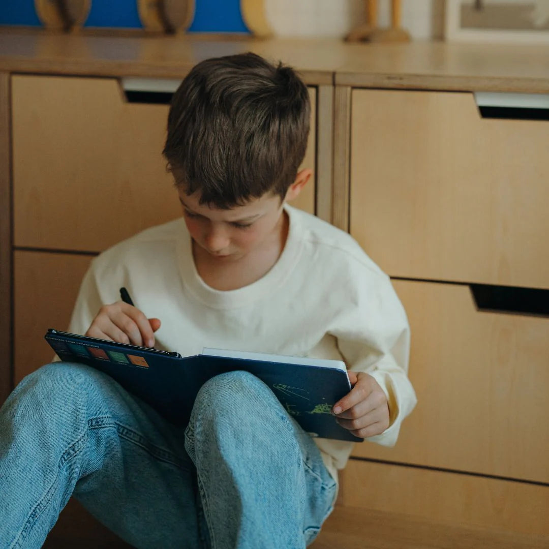Child sitting on the floor with a book and pen in a home setting
