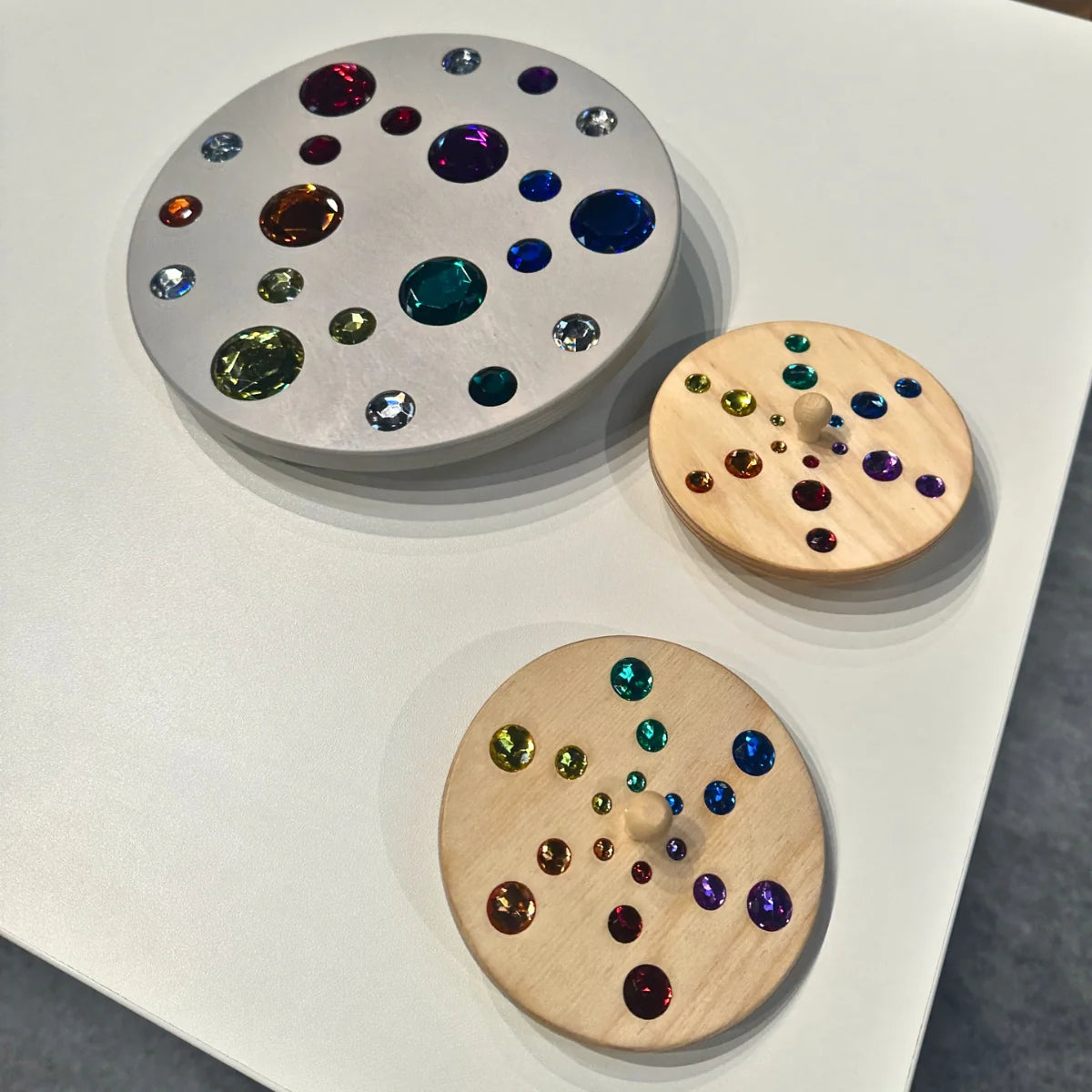 Three circular objects with embedded colorful gemstones on a white surface