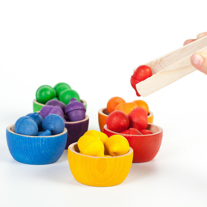 Colorful wooden toy set with bowls and marbles on a white background