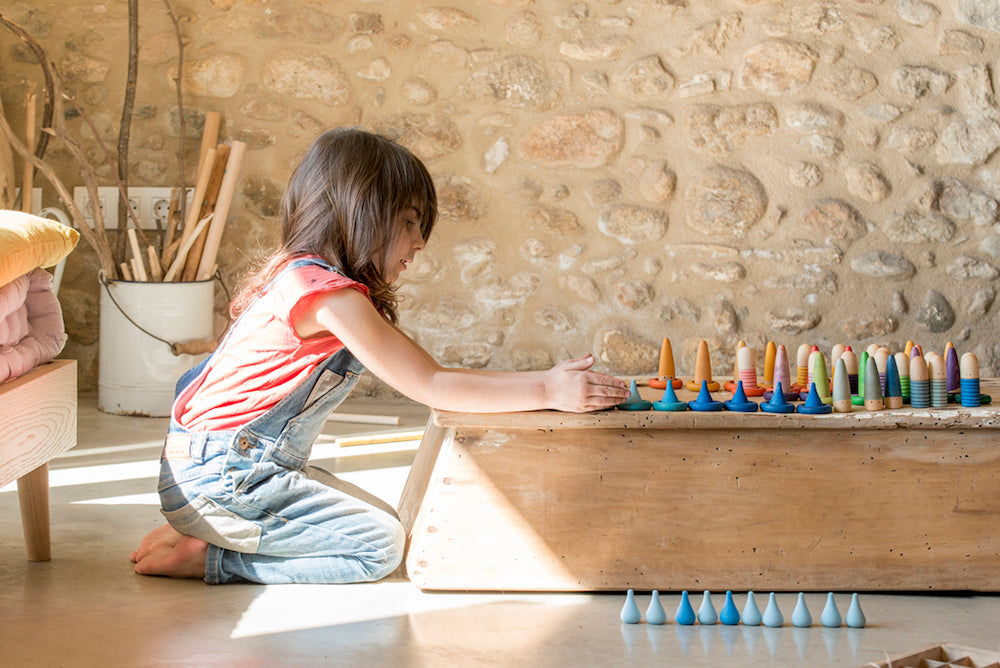 Child playing with colorful wooden toys on a wooden table against a stone wall.
