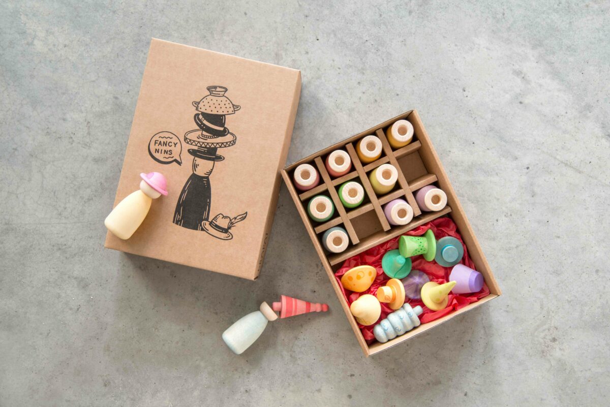 Colorful toy nins  in an open box with a cardboard box featuring illustrations on a gray surface.