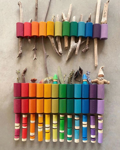 Colorful wooden toy xylophone made from sticks and crayon holders on a gray wall.