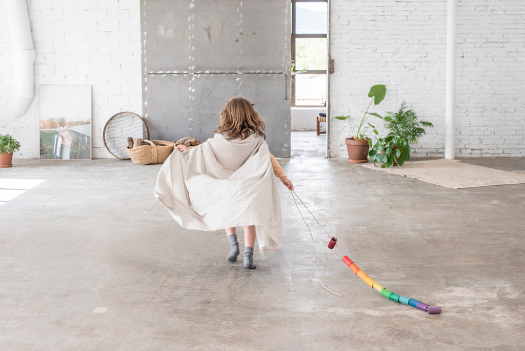 Child playing with a rainbow toy in a room with white walls and wooden floor.