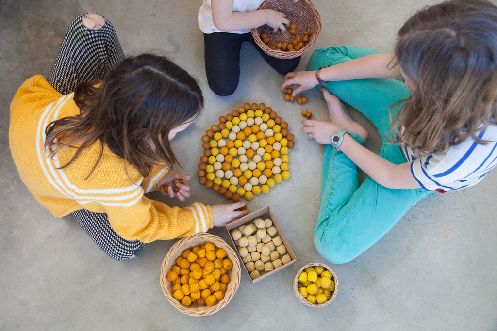 Three children playing with small baskets of yellow objects on a gray floor.