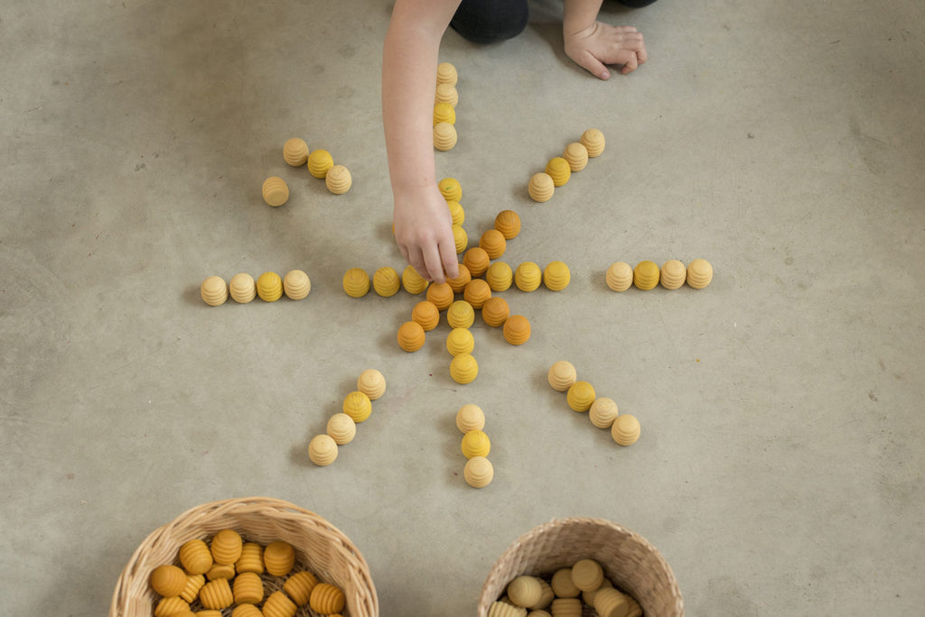 Hand arranging yellow and orange balls on a concrete floor with two baskets nearby.