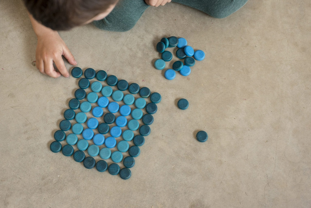 Child arranging blue circular objects on a beige carpet