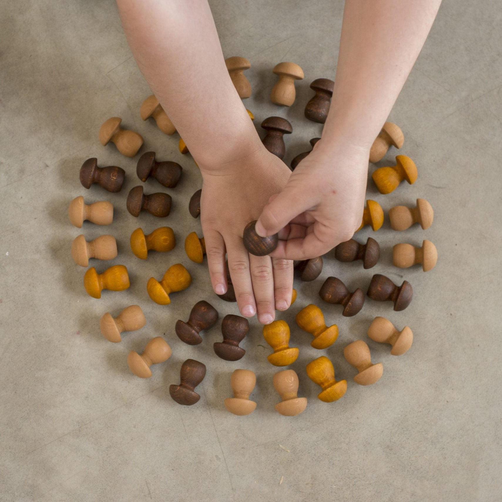 Hands interacting with a collection of wooden mushrooms on a beige surface