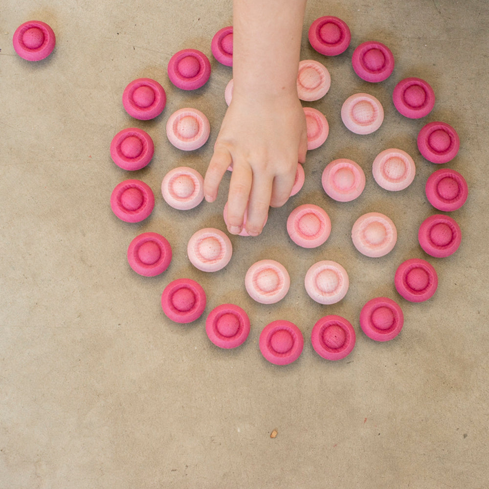 Child's hand reaching towards pink circular objects arranged in a pattern on a beige surface.
