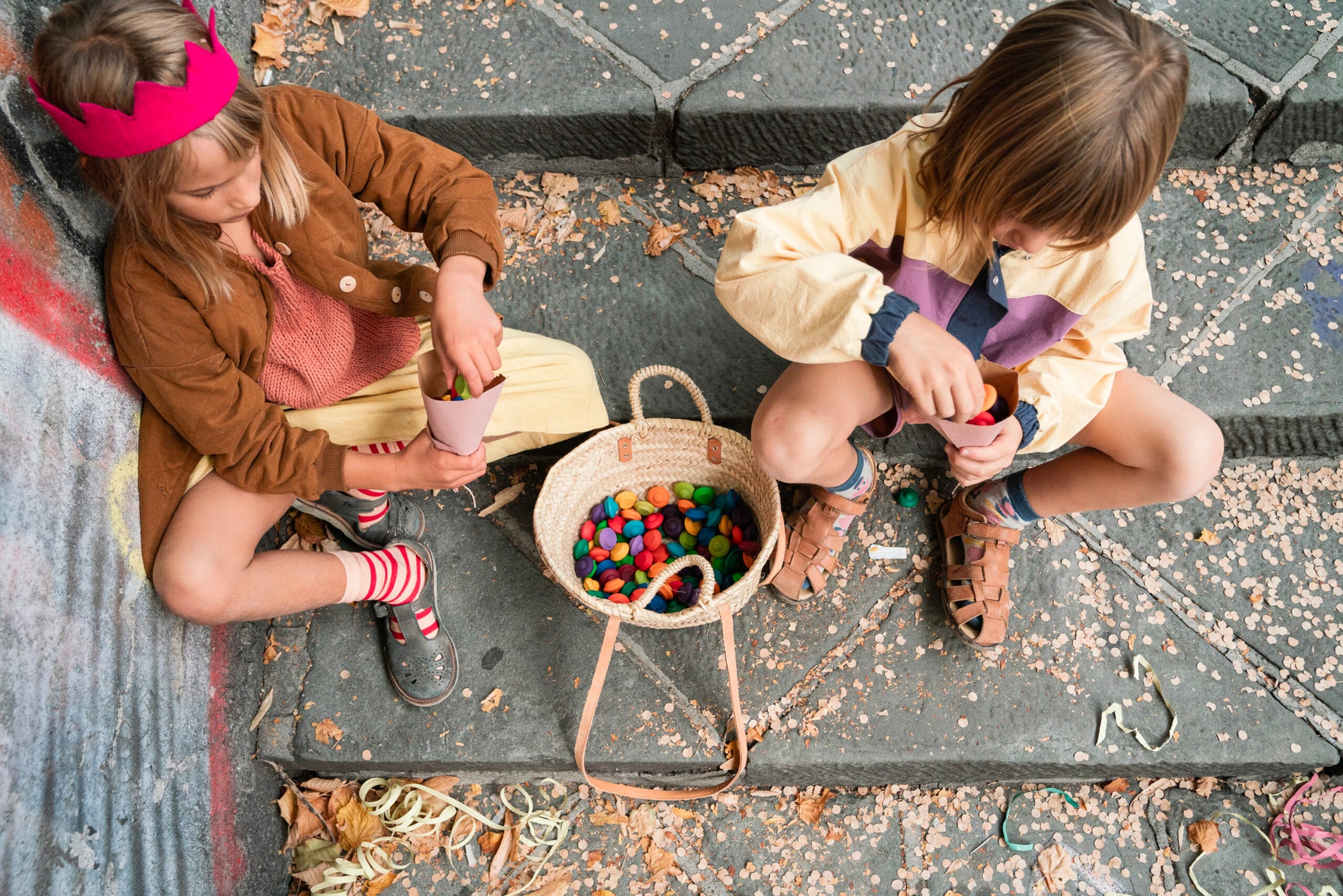 Two children sitting on a curb with a basket of colorful items