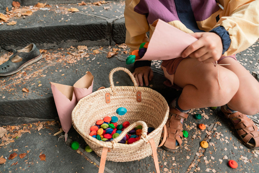 Person sitting on steps with a woven basket of colorful toys and pink paper cones.