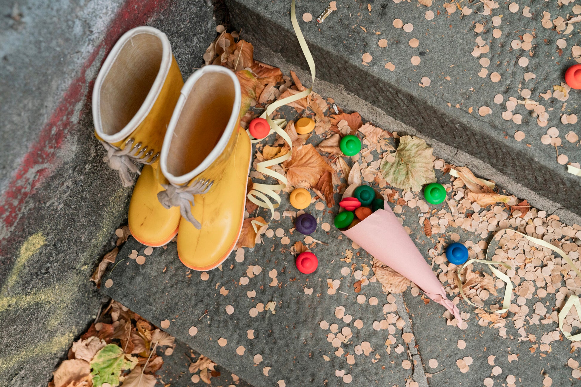 Yellow boots on a concrete surface with colorful candy and leaves.