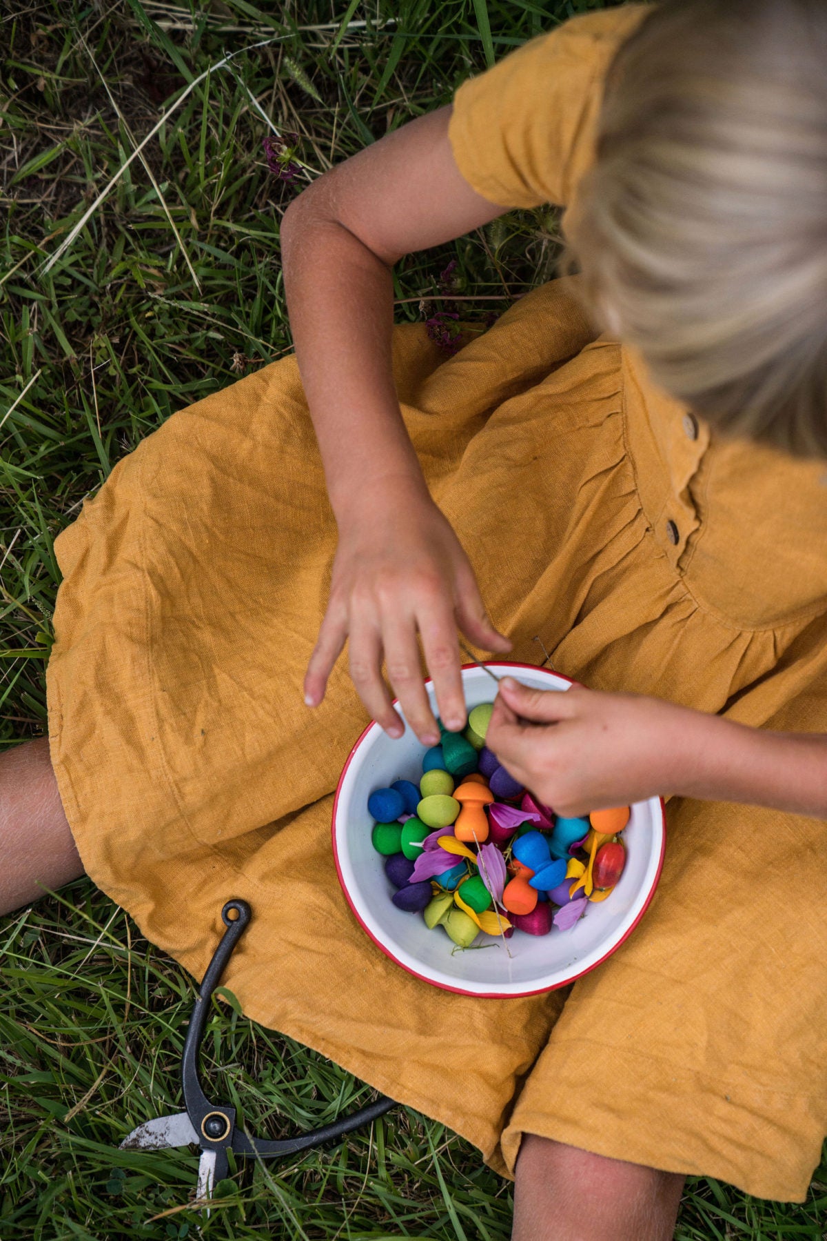 Child in a yellow dress playing with colorful toys in a white bowl on grass