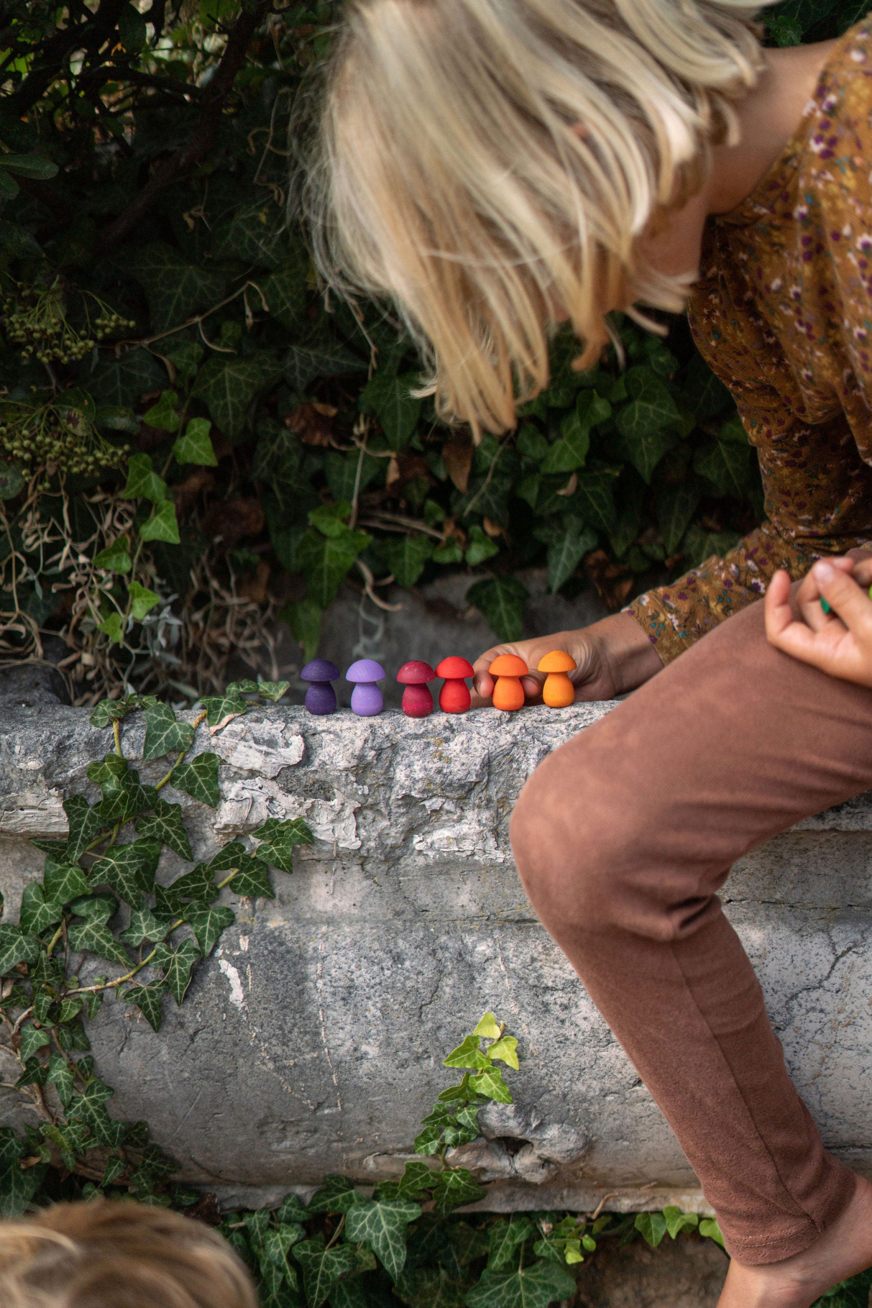 Person standing on a stone ledge with colorful objects and greenery around
