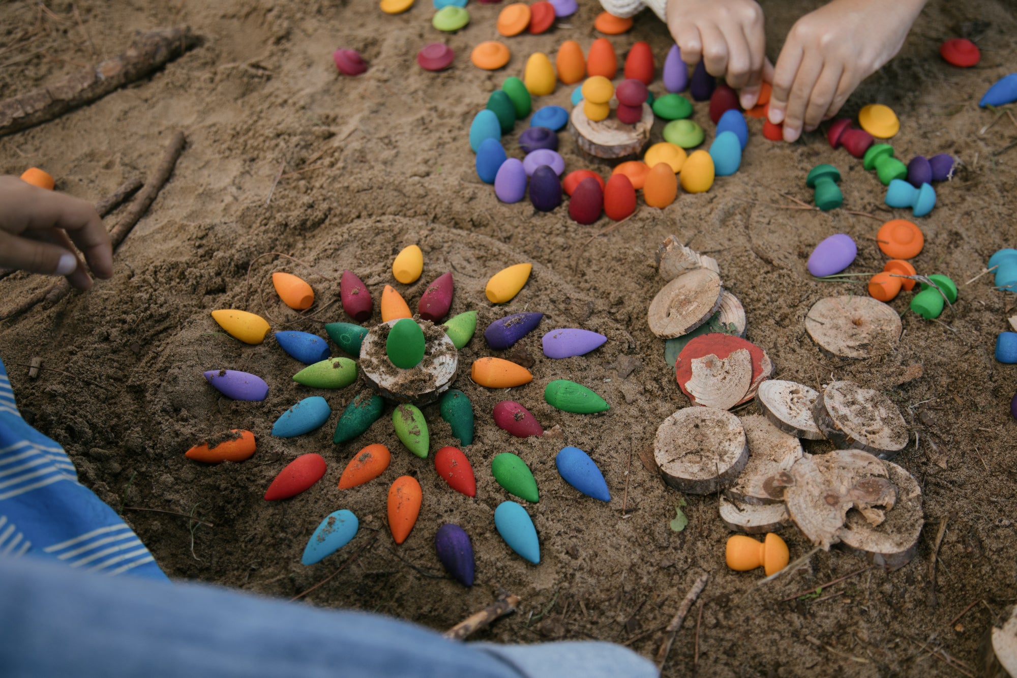 Colorful mandala art on sand with hands arranging stones