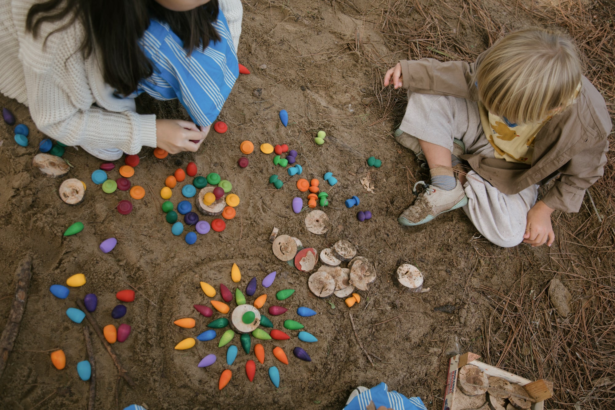 Two children playing with colorful stones on a sandy surface