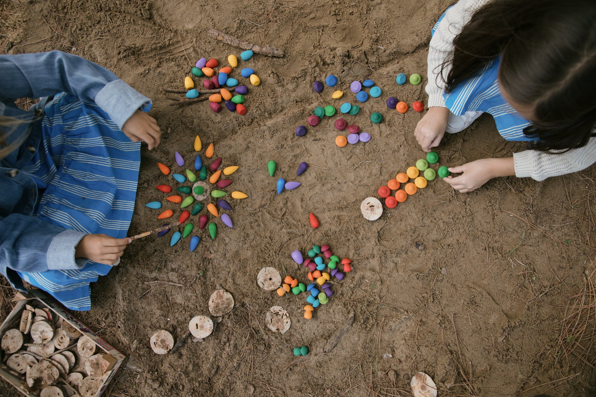 Two children playing with colorful stones on a sandy surface
