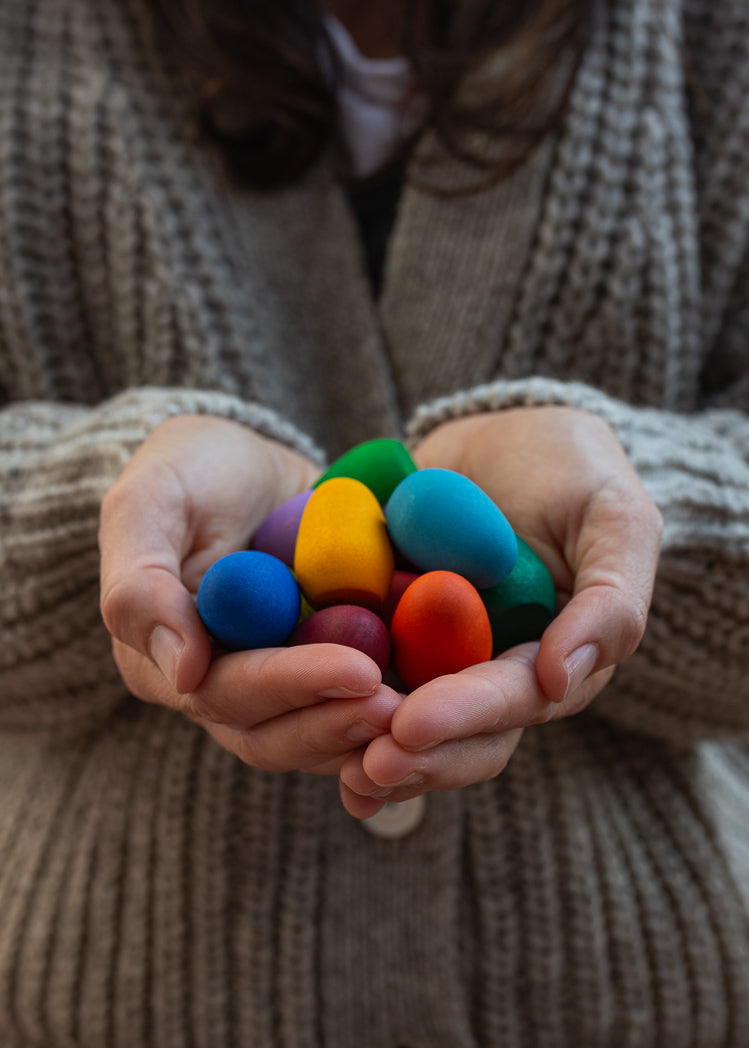 Person holding colorful clay models in their hands, wearing a brown sweater.