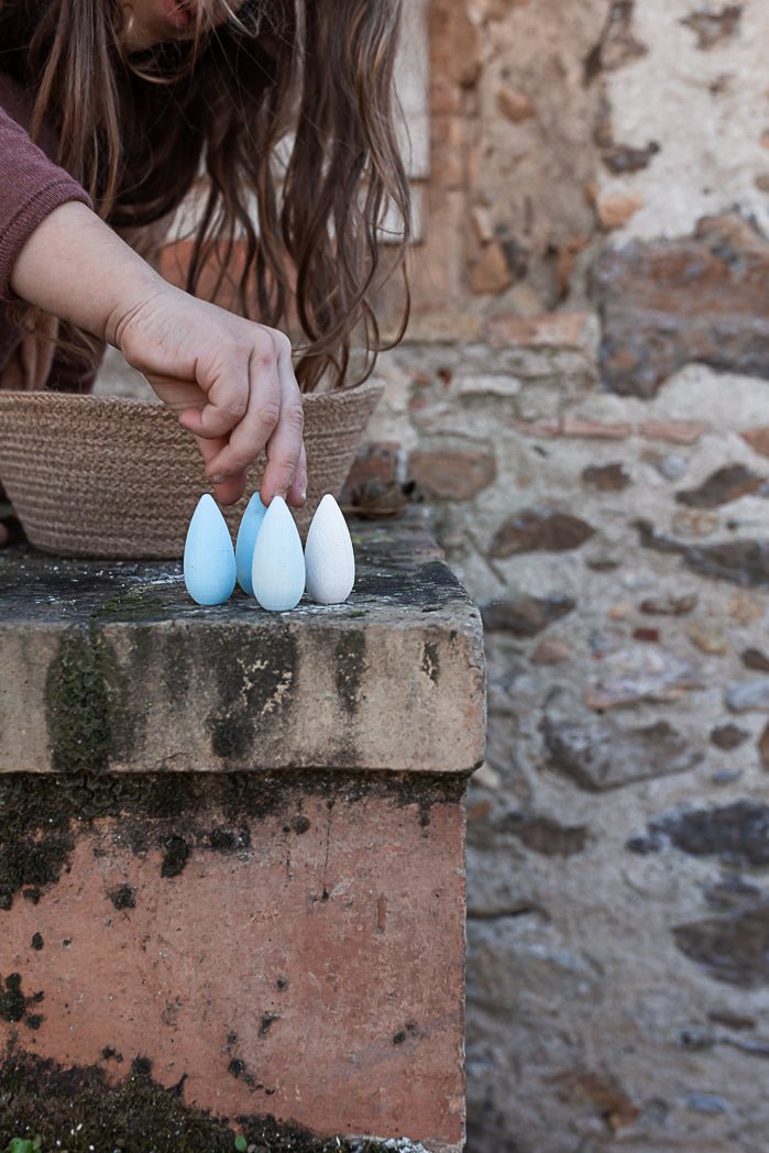 Person arranging wooden eggs on a stone surface with a rustic background