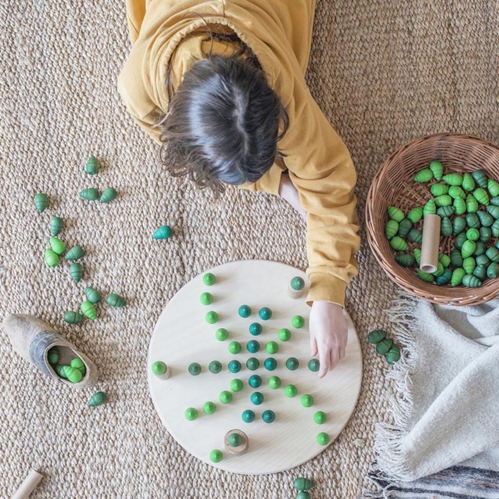Child playing with green beads on a white board on a beige carpet