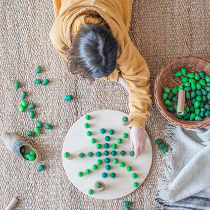 Child playing with green beads on a white board on a beige carpet