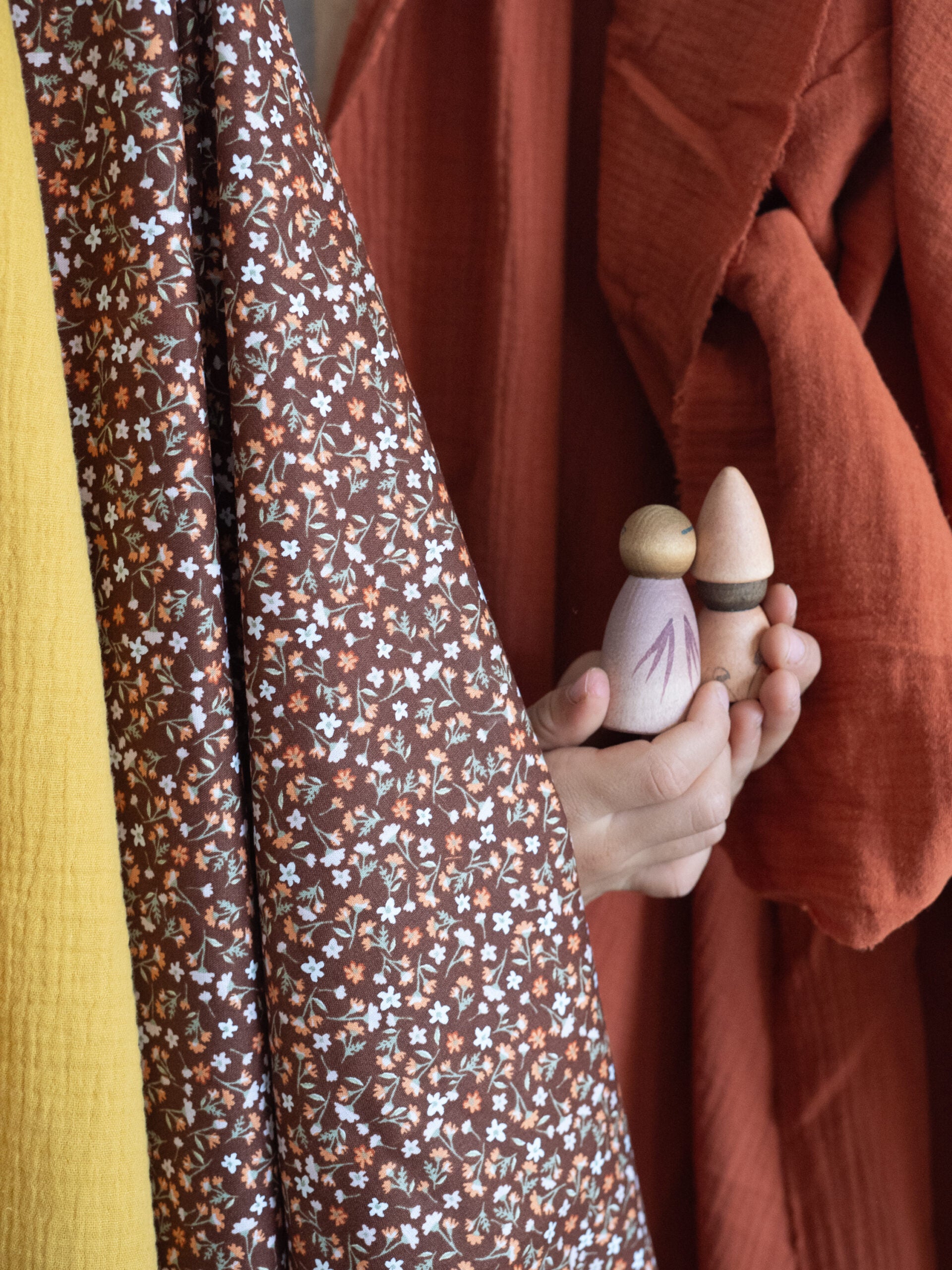 Person holding a small wooden object with a pattern, wearing a brown floral dress.