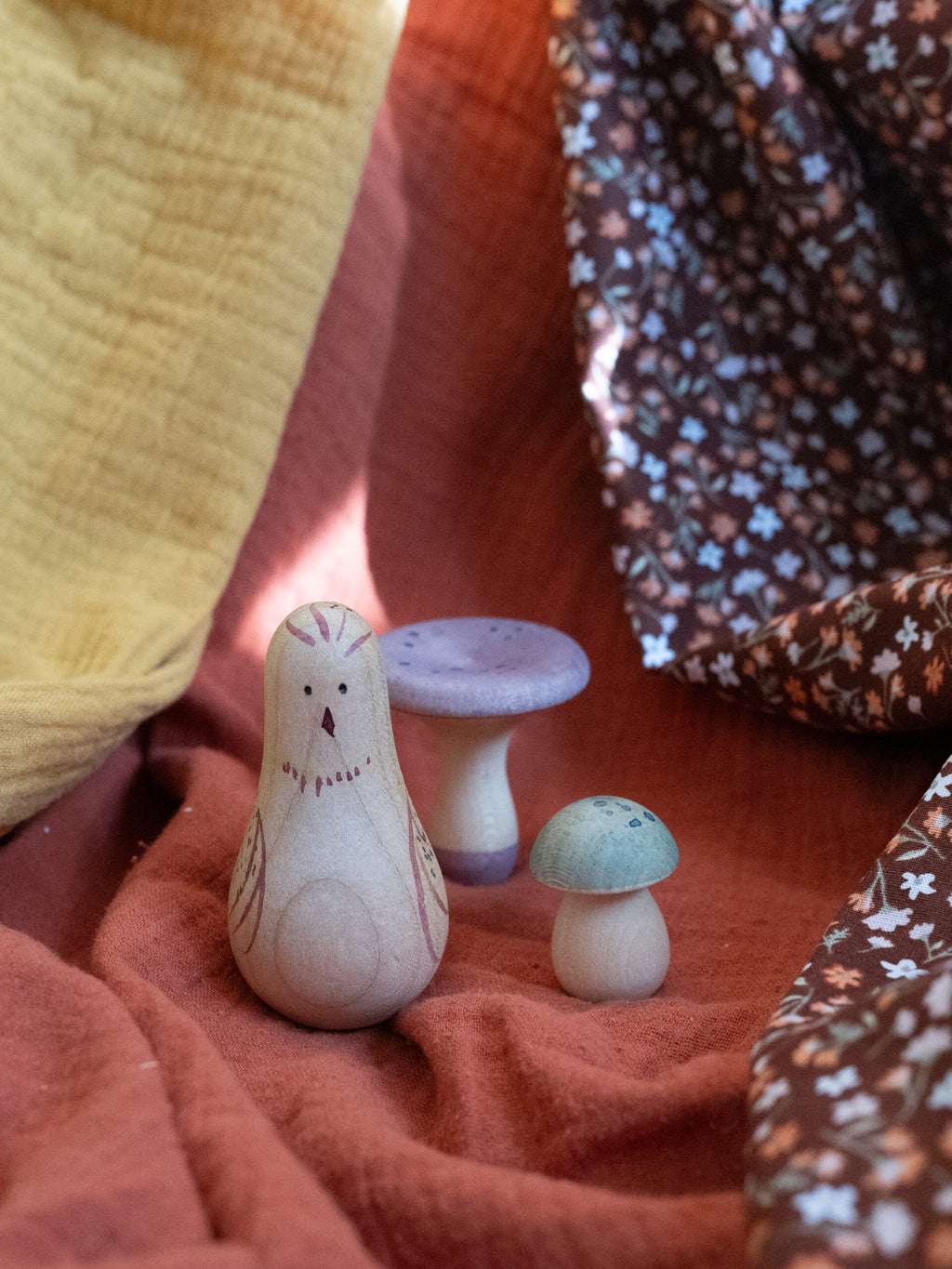 Wooden owl figurine and two small mushroom-shaped objects on a textured surface